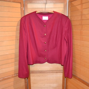 Op de afbeelding: Een bordeauxrode blazer met een ronde halslijn en gouden knopen. De blazer heeft lange mouwen en een verkorte lengte.