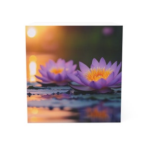 May include: Two purple water lilies with yellow centers float on a still pond at sunset. The water reflects the warm orange light of the setting sun.