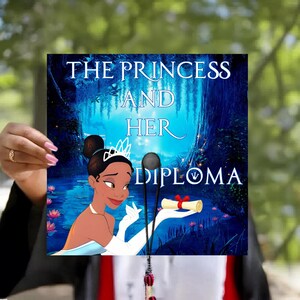 May include: A square graduation cap topper featuring a dark blue swamp background with water lilies and the text THE PRINCESS AND HER DIPLOMA. A cartoon character with a white tiara and gloves holds a rolled diploma tied with a red ribbon.