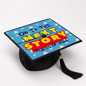 Op de afbeelding: Zwarte afstudeerhoed met een hemelsblauwe bovenkant met de tekst "ON TO THE NEXT STORY CLASS OF 2026" in geel en rood. De hoed heeft een zwarte kwast met gouden accenten.