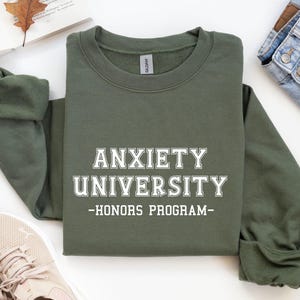 May include: Green sweatshirt with white text that reads "Anxiety University - Honors Program".
