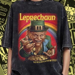 May include: Black t-shirt featuring a colorful illustration of a leprechaun with a green hat, gold coins, and the text "Leprechaun." The shirt has a vintage, distressed look. The text "THEY'RE ALWAYS AFTER ME GOLD!" is also visible.