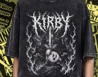 Puede incluir: Una camiseta negra con lavado ácido que presenta un estampado gráfico blanco del personaje Kirby sosteniendo una espada en alto. El diseño incluye el texto estilizado KIRBY sobre el personaje, rodeado de llamas y un fondo de castillo.