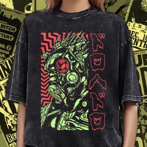 Może przedstawiać: Czarny t-shirt z efektem sprania kwasem, ozdobiony grafiką przedstawiającą postać w masce przeciwgazowej w kolorach limonkowym i czerwonym. Wzór zawiera czerwony zygzak po lewej stronie oraz japoński tekst katakana w kolorze czerwonym po prawej.