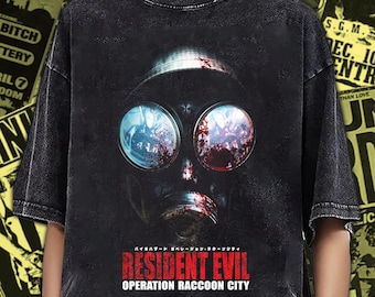 Puede incluir: Una camiseta negra con efecto lavado al ácido que presenta un gráfico de una máscara de gas con lentes reflectantes. Debajo de la máscara, el texto dice Resident Evil Operation Raccoon City en letras rojas y blancas. Tiene mangas cortas y cuello redondo.