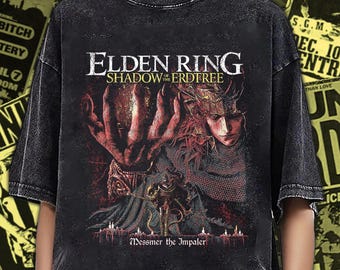 Puede incluir: Una camiseta gris carbón con efecto lavado al ácido que presenta un estampado gráfico del videojuego Elden Ring Shadow of the Erdtree. El diseño muestra una mano grande, un personaje de pelo rojo y el texto Messmer the Impaler sobre velas.
