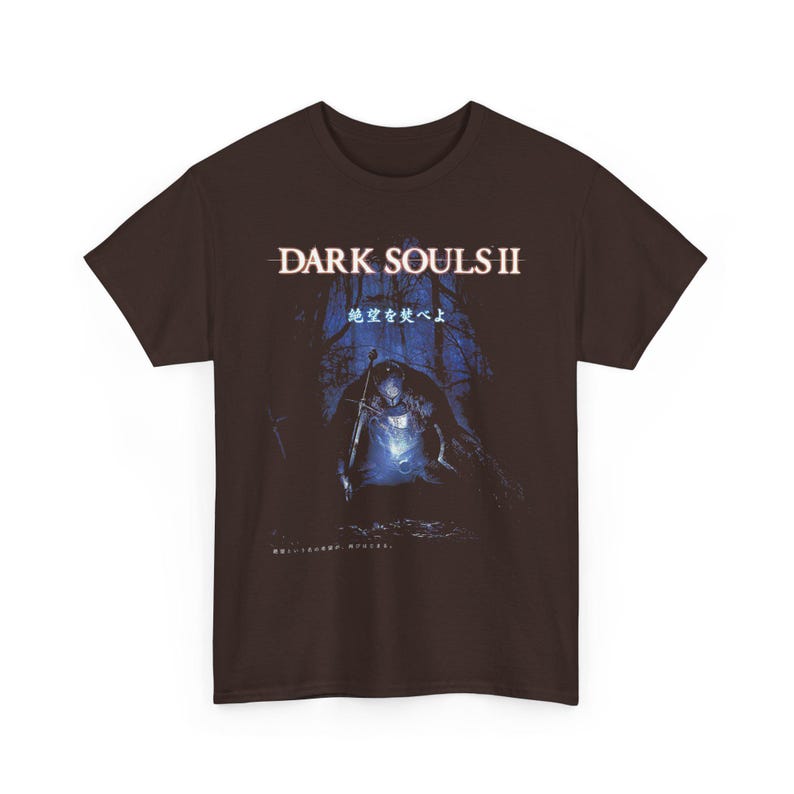 May include: Brown t-shirt featuring the text "DARK SOULS II" above an illustration of a knight in a dark forest. The graphic is in shades of blue and white, with Japanese text below the main title.