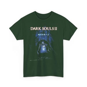 May include: Dark green t-shirt featuring the text "DARK SOULS II" above a blue and black graphic of a figure with a sword in a forest setting. Japanese text is also present.