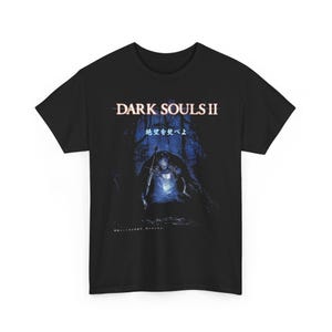 May include: Black t-shirt featuring the text "DARK SOULS II" above an illustration of a knight in a dark forest. The image has a blue and white color scheme, with Japanese text below the title.