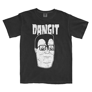 May include: A black short-sleeve t-shirt featuring a white distressed graphic of a man's face wearing glasses with a prominent forehead cowlick. Above the face, the word DANGIT is printed in a bold, white, distressed, capital letter font.