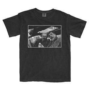 May include: Black t-shirt featuring a black and white image of two men in a car. The image shows the men holding a can and looking at the camera. The t-shirt is made of a soft material.