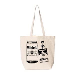 May include: Cream-colored tote bag featuring a black and white graphic design. The design includes a beer can labeled "Miidelo", a cartoon figure, and a pack of "Miiboro" cigarettes. The bag has two handles.