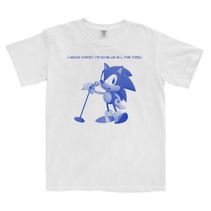 Puede incluir: Camiseta blanca con un gráfico azul de un erizo de dibujos animados cantando en un micrófono. El texto sobre el gráfico dice "JESUS CHRIST, I'M SO BLUE ALL THE TIME."