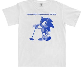 Op de afbeelding: Wit t-shirt met een blauwe afbeelding van een tekenfilmegel die in een microfoon zingt. De tekst boven de afbeelding luidt "JESUS CHRIST, I'M SO BLUE ALL THE TIME."