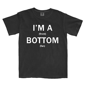 May include: Black t-shirt with the white text "I'M A (front) BOTTOM (fan)". The shirt has a crew neck and short sleeves. The fabric appears to be pre-shrunk cotton.