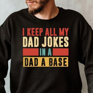 May include: A black sweatshirt with a vintage-style graphic that reads "I keep all my dad jokes in a dad a base".
