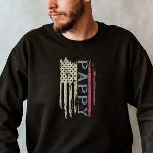 May include: A black sweatshirt with a distressed American flag design and the word "PAPPY" written vertically down the flag.