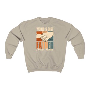 May include: A tan sweatshirt with a retro-style graphic that says "World's Best Father I Mean Father" with a picture of two hands holding each other.