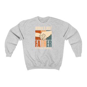 May include: Gray sweatshirt with a retro-style graphic that says "World's Best Father" with a hand holding a smaller hand. The text "I Mean Father" is below the graphic.