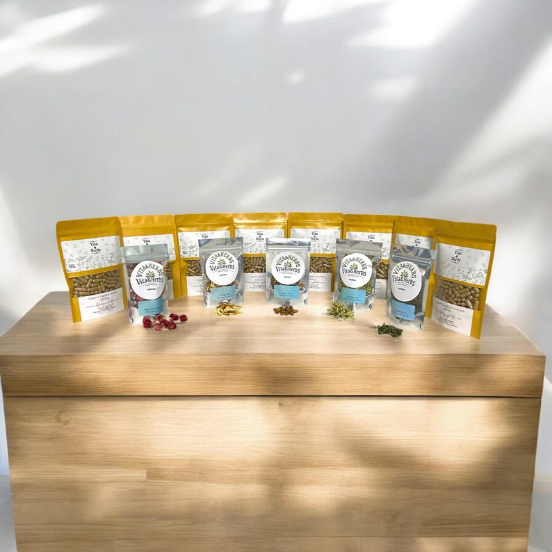 May include: A display of several pouches and bags of Vitaherbs supplements, arranged on a wooden surface. The bags are gold and clear, with the Vitaherbs logo and product information visible. Various herbs and berries are scattered in front of the bags.