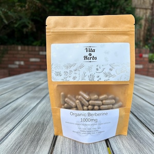 May include: A brown paper bag with a white label that says "Vita & Herbs" and "Organic Berberine 1000mg". The bag contains a clear plastic bag filled with brown capsules.