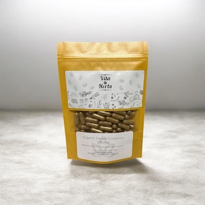 May include: A gold-colored pouch of Vita Herbs Organic Ceylon Cinnamon capsules. The clear window displays brown capsules. The label reads "Organic Ceylon Cinnamon 1000mg". The top label has the Vita Herbs logo.
