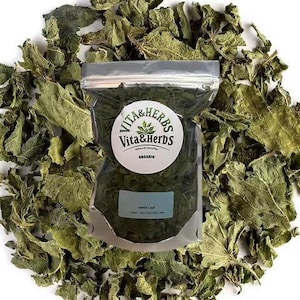 Könnte beinhalten: Ein klarer Plastikbeutel mit getrockneten grünen Blättern, beschriftet mit "Nettle Leaf" und "Vita & Herbs Organic", liegt auf einem Bett aus ähnlichen getrockneten Blättern. Die Blätter sind von gedämpfter grüner Farbe, der Beutel ist mit einem Reißverschluss verschlossen.