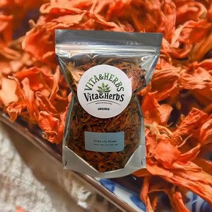 Peut inclure: Un sac en plastique transparent contenant des fleurs de lys séchées, étiqueté "Vita & Herbs Organic". Le sac est posé sur un fond de fleurs séchées orange vif sur un plateau décoratif. L'étiquette indique "Dried Lily Flower".
