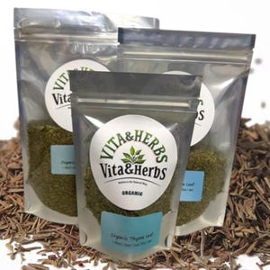 May include: Three clear plastic pouches of organic thyme leaf, labeled "Vita & Herbs." The pouches are filled with green herbs and are sealed with a silver zipper. A pile of dried thyme is in the background.