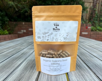 May include: A brown paper stand-up pouch containing brown capsules. The label features the text Vita & Herbs, Organic Guarana Seed, 1000mg, ingredients, and quantity options. The pouch has a clear window revealing the capsules inside.