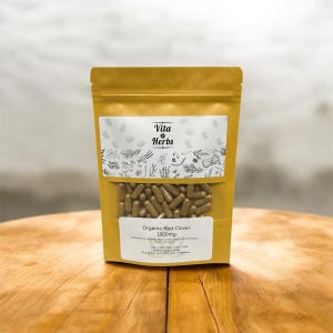 May include: A brown paper bag of Vita Herbs Organic Red Clover 1000mg capsules. The bag has a clear window showing the capsules. The label includes the brand name and botanical illustrations. The bag is sitting on a wooden surface.