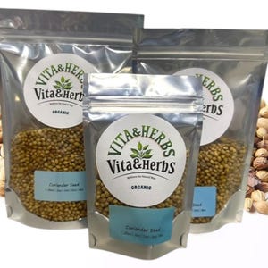 May include: Three clear, resealable bags of coriander seeds, labeled "Vita & Herbs Organic." The bags are filled with small, round, tan seeds. A pile of coriander seeds is scattered around the bags.