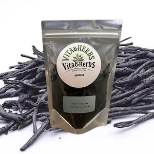 Może przedstawiać: Przezroczysta plastikowa torba z organiczną herbatą Vita & Herbs Needle Budding, z białą etykietą i okrągłym logo. Torba otoczona jest stosem ciemnych, suszonych liści herbaty. Tło jest białe.