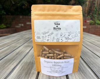 May include: A brown kraft paper stand-up pouch containing brown capsules. The label features the text Vita & Herbs, Organic Burdock Root, 1000mg, and a botanical illustration. A clear window in the center of the pouch reveals the capsules inside.