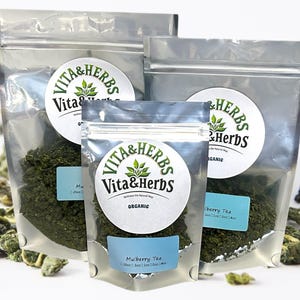 Könnte beinhalten: Drei silberne wiederverschließbare Beutel mit Bio-Tee. Die Beutel sind mit einem grünen Kreislogo mit der Aufschrift "Vita & Herbs" versehen. Der kleinste Beutel ist mit "Mulberry Tea" beschriftet. Der mittlere Beutel ist mit "Mulberry Tea" beschriftet. Der größte Beutel ist mit "Elderberry Tea" beschriftet.