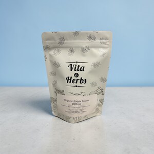 May include: A white pouch with the text "Vita & Herbs" and "Organic Purple Potato 1000mg". The pouch has a leaf pattern and is set against a light blue backdrop.