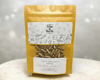 May include: A golden-yellow pouch with a clear window, filled with brown capsules. The pouch has two white labels with text and botanical illustrations. The top label reads "Vita & Herbs." The bottom label says "Organic Sarsaparilla 1000mg."