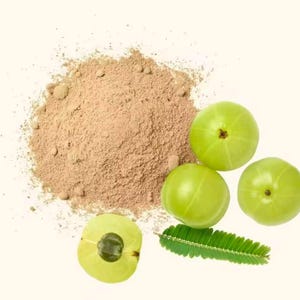 May include: A top-down shot features a pile of brown powder next to several green fruits and a green leaf. One fruit is sliced open, revealing its interior. The background is a solid, off-white color.