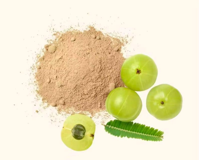 May include: A top-down shot features a pile of brown powder next to several green fruits and a green leaf. One fruit is sliced open, revealing its interior. The background is a solid, off-white color.