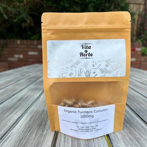 May include: A brown paper bag with a white label that says "Vita & Herbs" and "Organic Turmeric Curcumin 1000mg". The bag contains a large number of capsules.