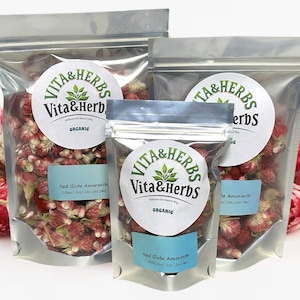 May include: Three clear, sealed bags of dried Red Globe Amaranth flowers. Each bag has a round label with the text "Vita & Herbs" and "Organic". The bags are filled with red flowers.