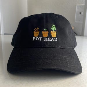 May include: Black baseball cap with an embroidered design of three potted plants and the text "POT HEAD".