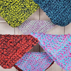 Puede incluir: Cuatro paños de cocina triangulares de ganchillo en diferentes combinaciones de colores: amarillo y negro, azul verdoso y negro, rosa y azul, y rojo y negro.