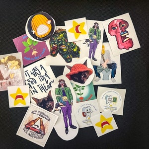 Op de afbeelding: Een verzameling diverse stickers met diverse ontwerpen. Sommige stickers bevatten illustraties van mensen, dieren en abstracte kunst. Andere tonen tekst zoals "Faith is like a seed" en "My vehicle, my choice". De stickers zijn in verschillende vormen en maten.