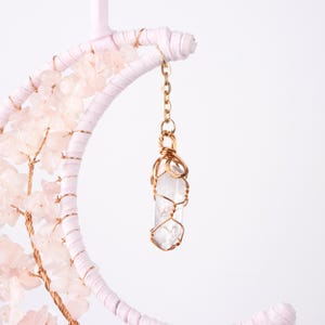 May include: A white crescent moon with pink crystals and a clear quartz crystal wrapped in gold wire hanging from it.