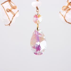 May include: A crystal chandelier with two iridescent crystal drops hanging from a gold wire. The crystal drops are faceted and reflect light.
