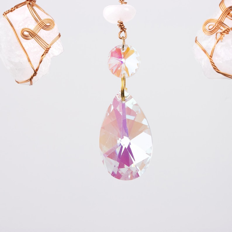 May include: A crystal chandelier with two iridescent crystal drops hanging from a gold wire. The crystal drops are faceted and reflect light.