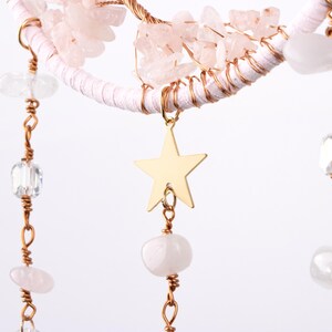 May include: A pink and gold dreamcatcher with a star charm and crystal beads hanging from it.