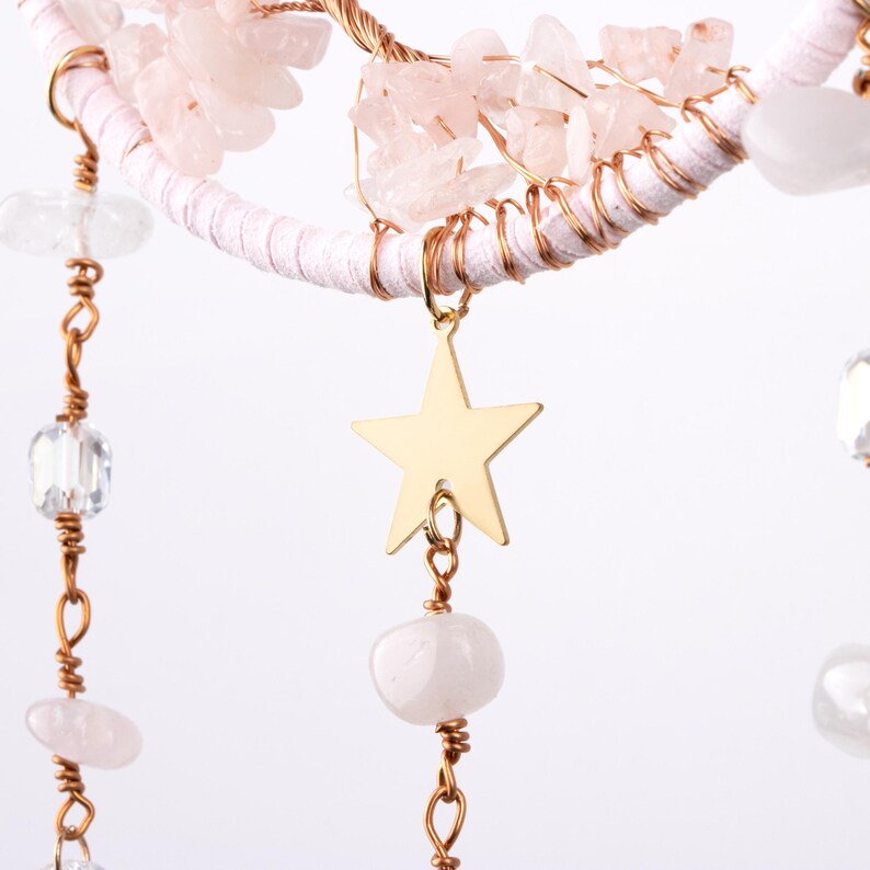 May include: A pink and gold dreamcatcher with a star charm and crystal beads hanging from it.