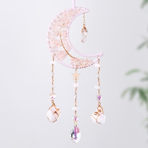 May include: A pink crystal moon dreamcatcher with gold wire and beads. The dreamcatcher has three strands of beads with crystal pendants and a gold star charm.